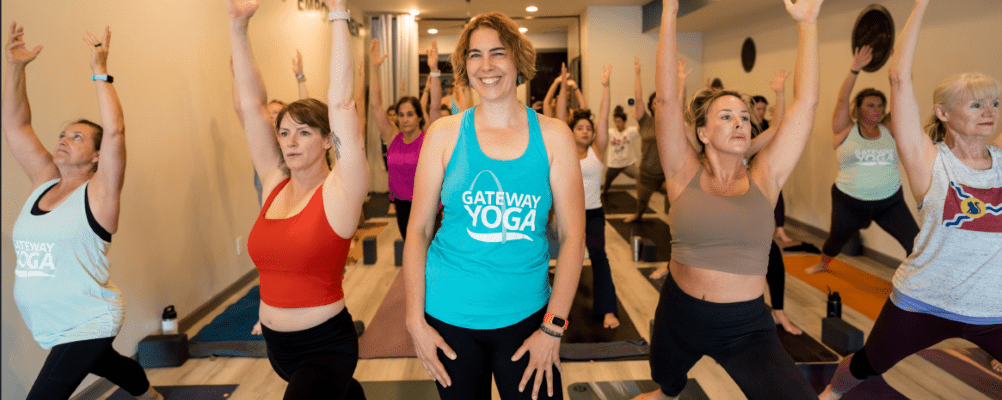 yoga class with teacher in center of photo. Students in warrior 1 pose.